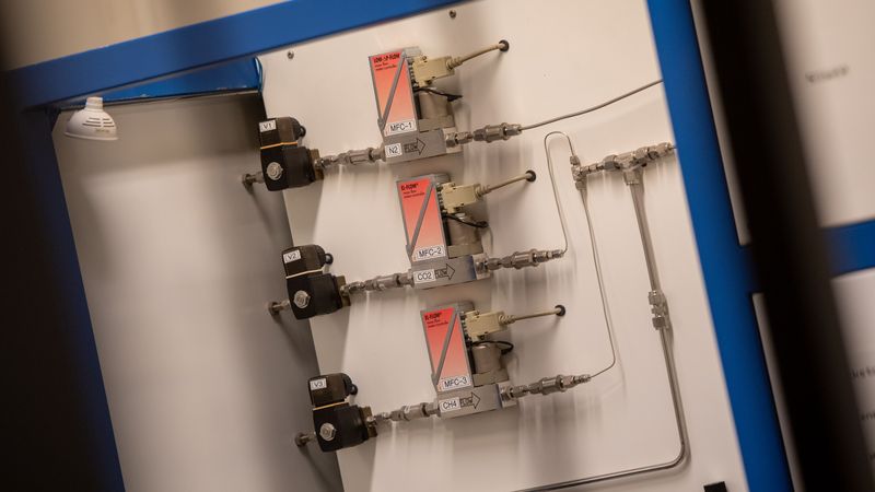 Drei gleich aussehende Module sind senkrecht an einer grauen Platte befestigt und mit Röhrchen und Steckern verbunden. 